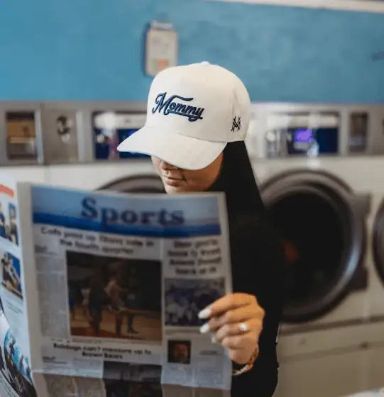 The Mad Hatter Company Mommy Snapback Hat, blue-check Mommy cap worn by a model reading a newspaper