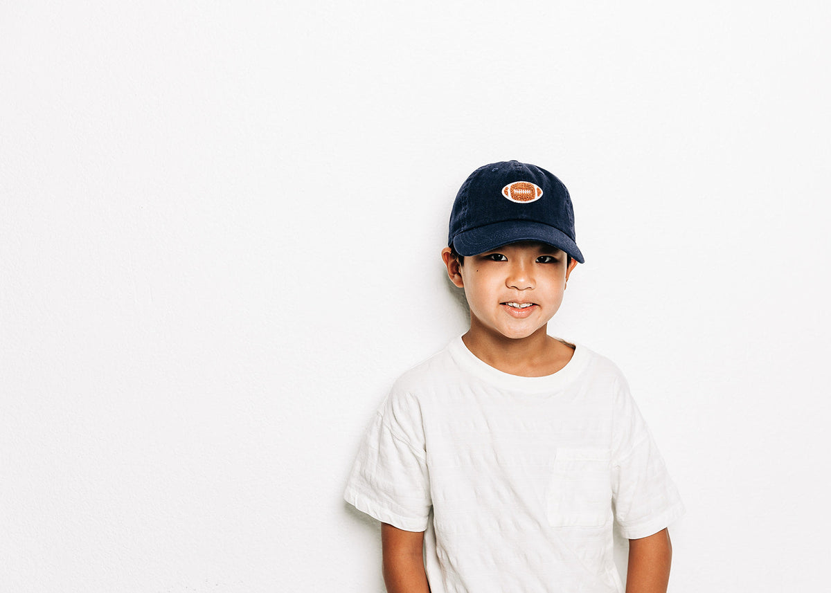 Rey To Z child wearing the Navy football-patch cap, full upper-body view