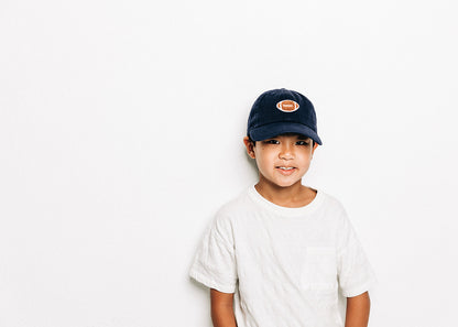 Rey To Z child wearing the Navy football-patch cap, full upper-body view