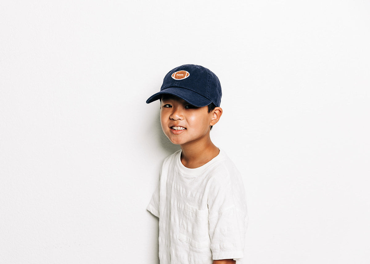 Rey To Z child wearing the Navy football-patch cap with a light T-shirt