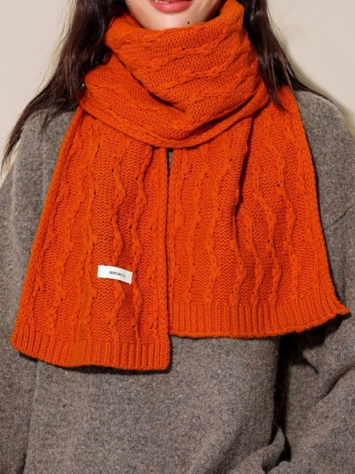 Unisex Wool Cozy Cable Knit Scarf — orange scarf wrapped around the neck over a gray coat