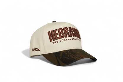 Destination Hat Co. Nebraska camo cap with beige crown and camouflage bill, angled view