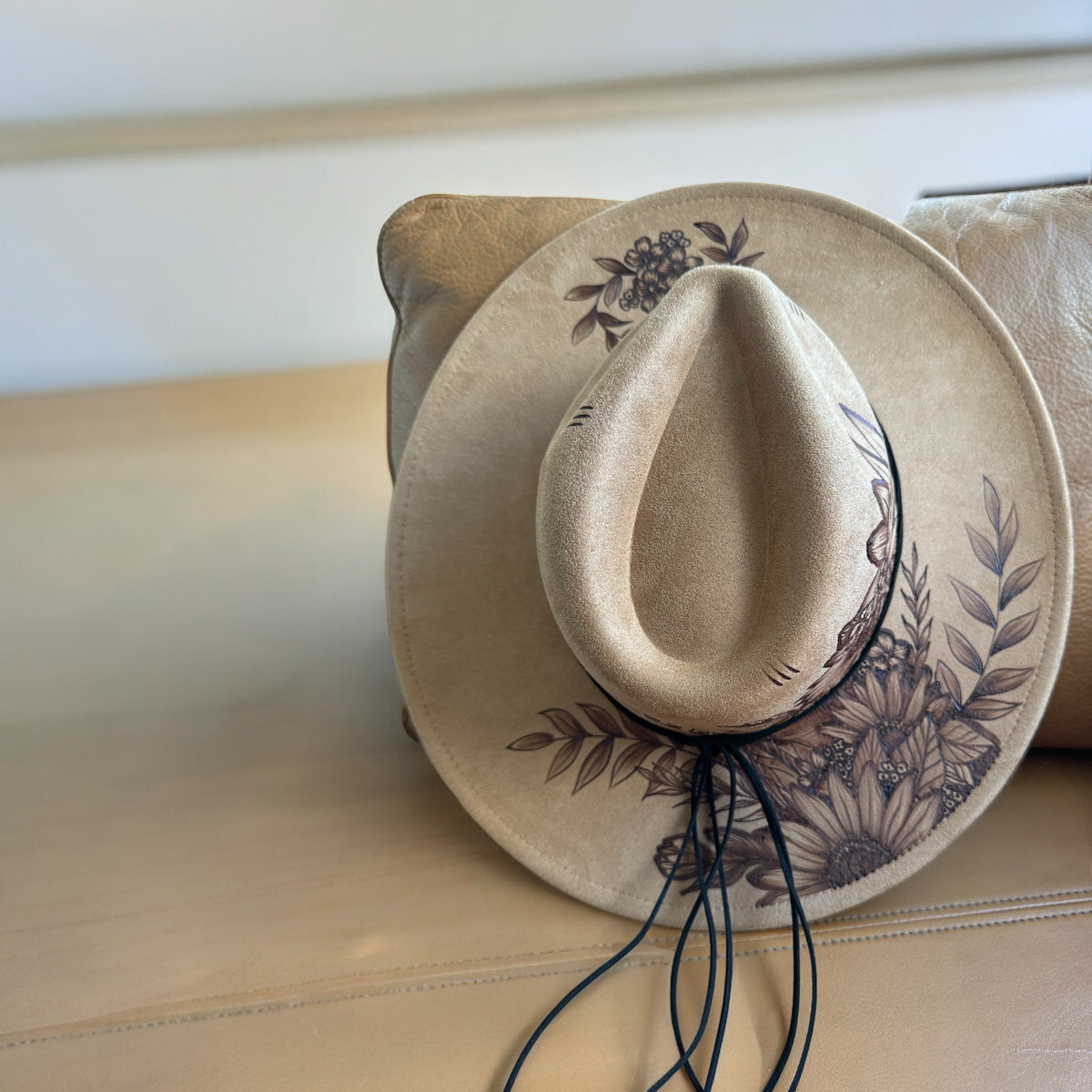 Beige Piper Whiteleaf wide-brim hat with burned leaf and flower artwork, overhead view