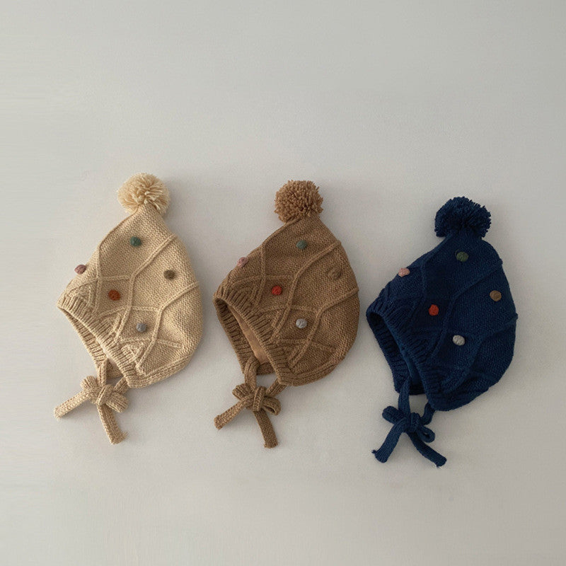 Three cable-knit pom pom earflap hats in beige coffee and navy tones