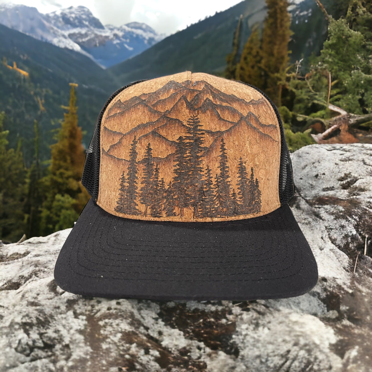Piper Cedar cork trucker with burned mountains and evergreen trees, photographed on a rock