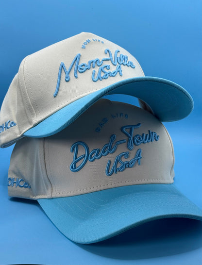 Two Mom-Ville caps arranged together, showing the light blue bills and script fronts