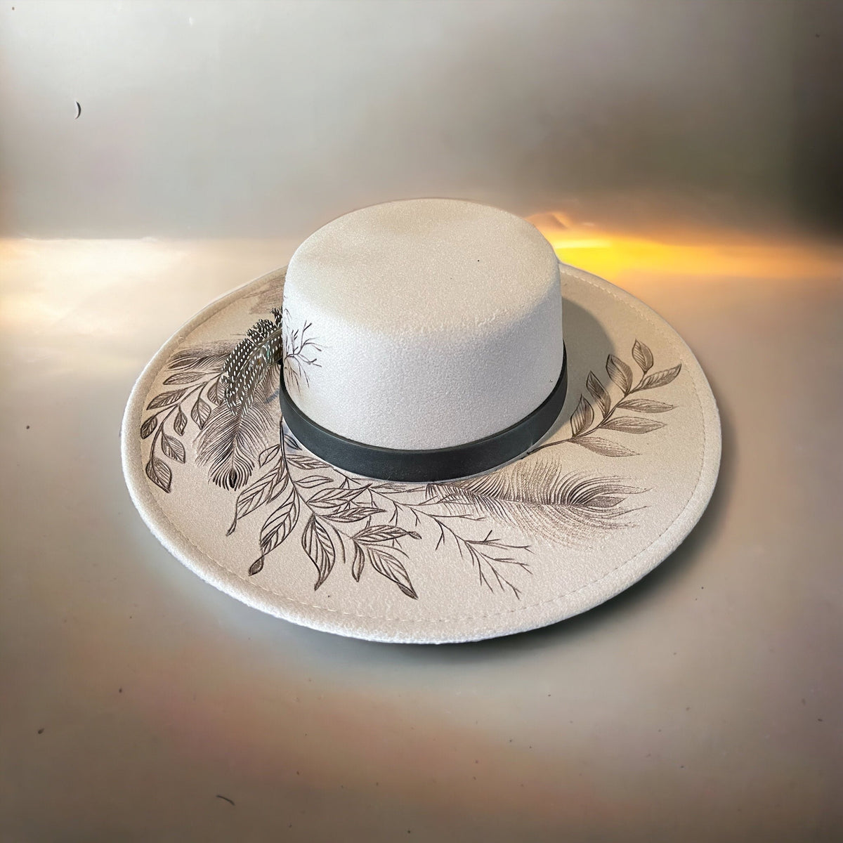 Ivory and beige bolero hat with burned leaf artwork photographed at sunset