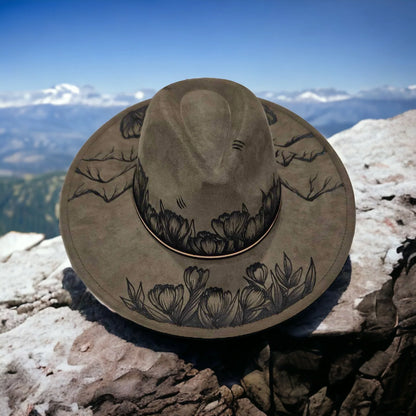 Olive Ridges & Roses wide-brim hat with mountain and rose artwork against a mountain backdrop