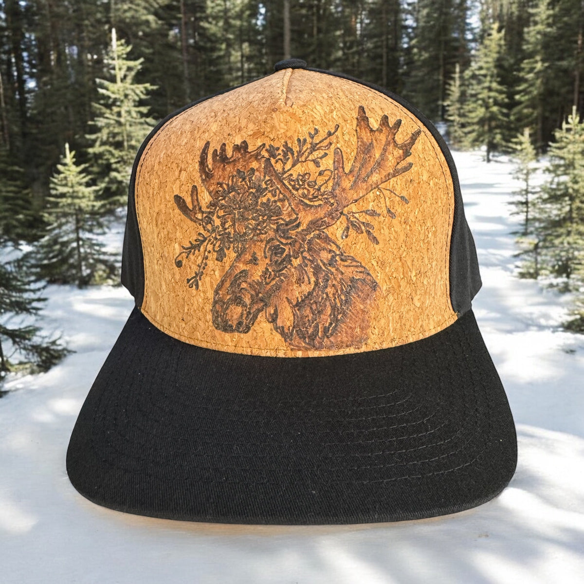 Piper Twigs cork trucker with burned moose artwork and a black bill against a snowy forest
