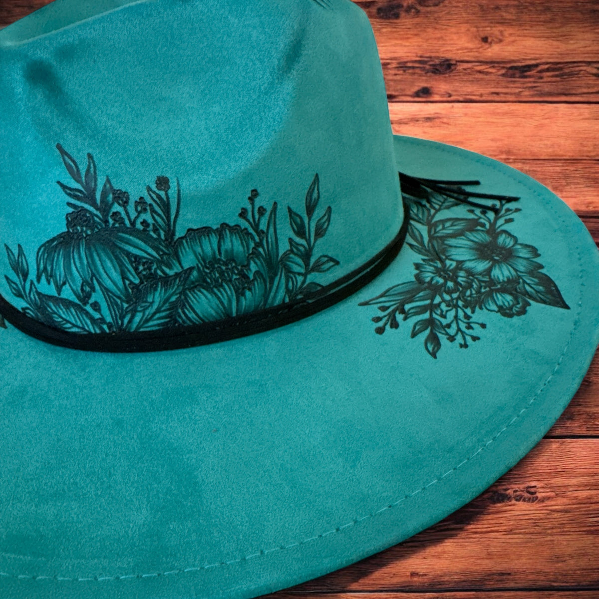 Close-up of the freehand floral artwork around the teal hat crown and brim