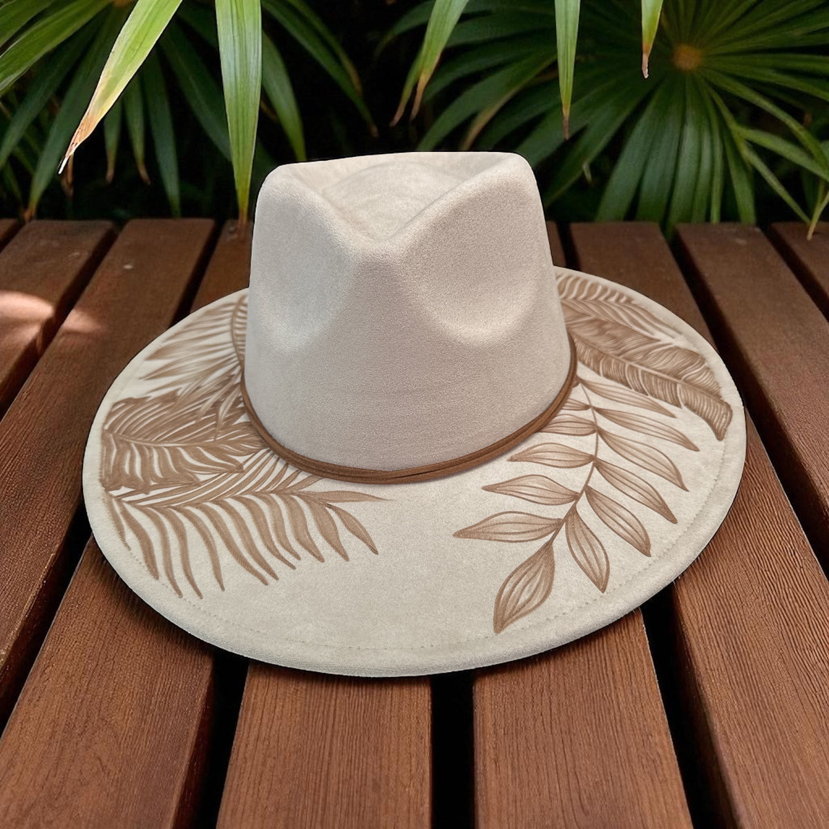 Ivory Floral fedora angled on a wooden table beneath green leaves
