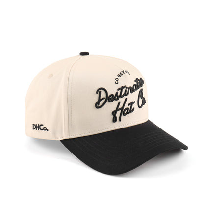 Destination Hat Co. Destination script cap with beige crown and black bill, angled view