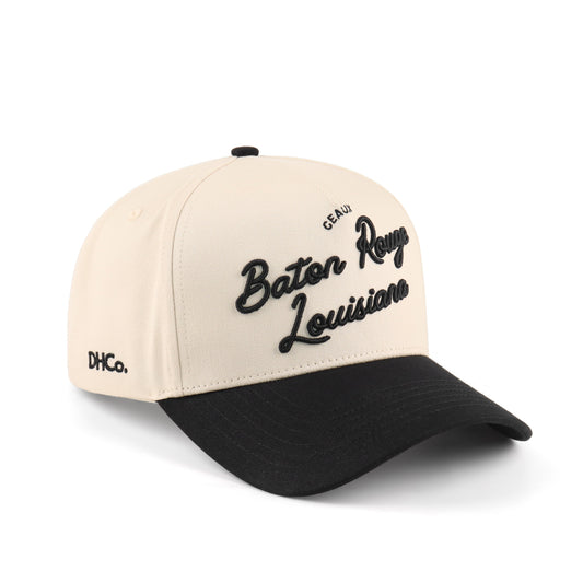 Destination Hat Co. Baton Rouge script cap with beige crown and black bill, angled view