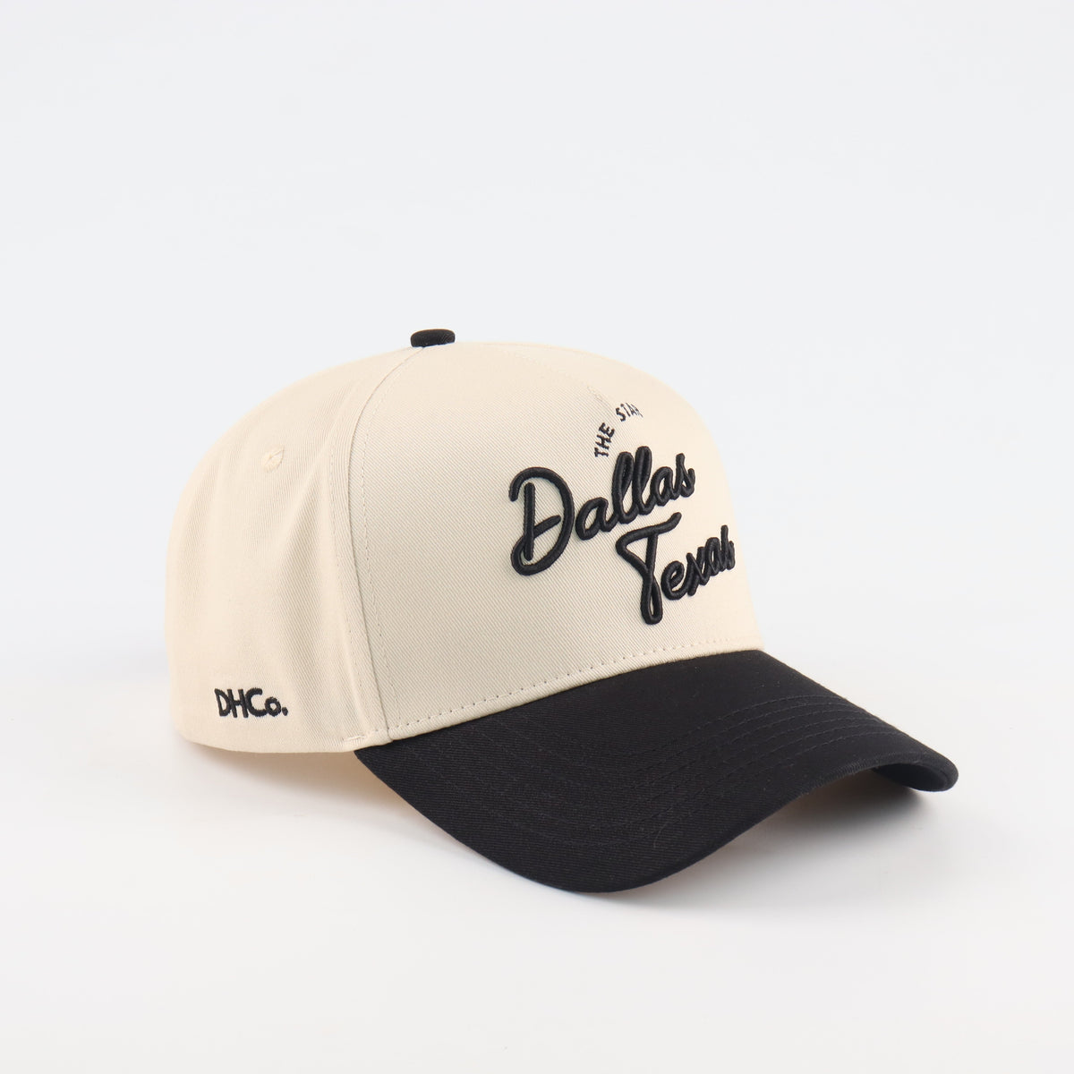 Destination Hat Co. Dallas script cap with beige crown and black bill, angled view