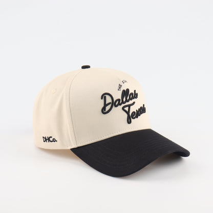 Destination Hat Co. Dallas script cap with beige crown and black bill, angled view