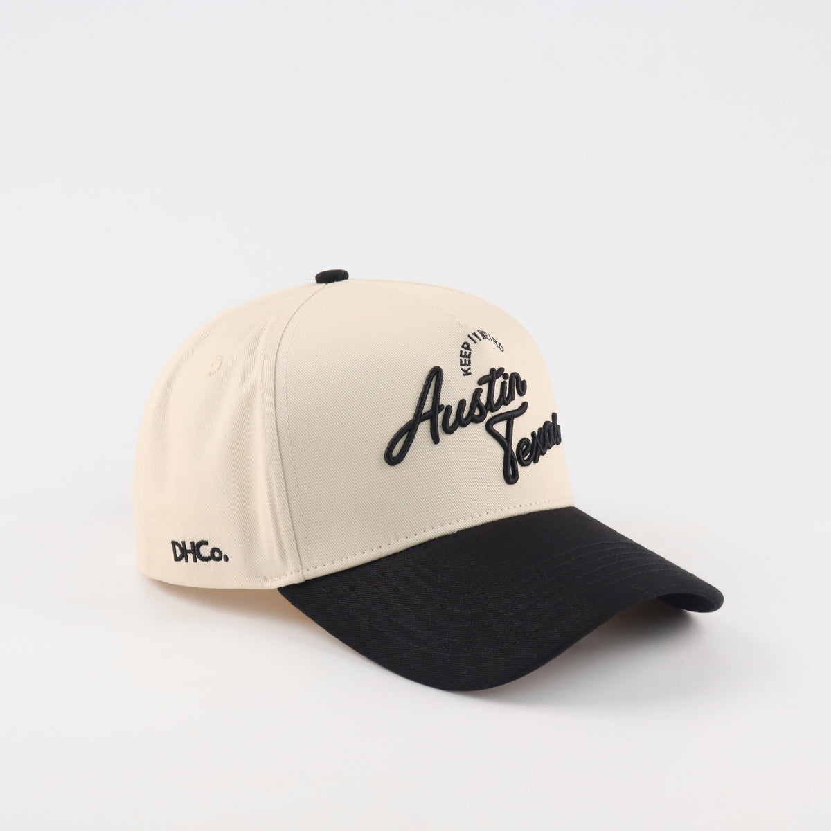 Destination Hat Co. Austin script cap with beige crown and black bill, angled view