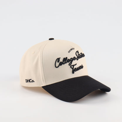 Destination Hat Co. College Station script cap with beige crown and black bill, angled view