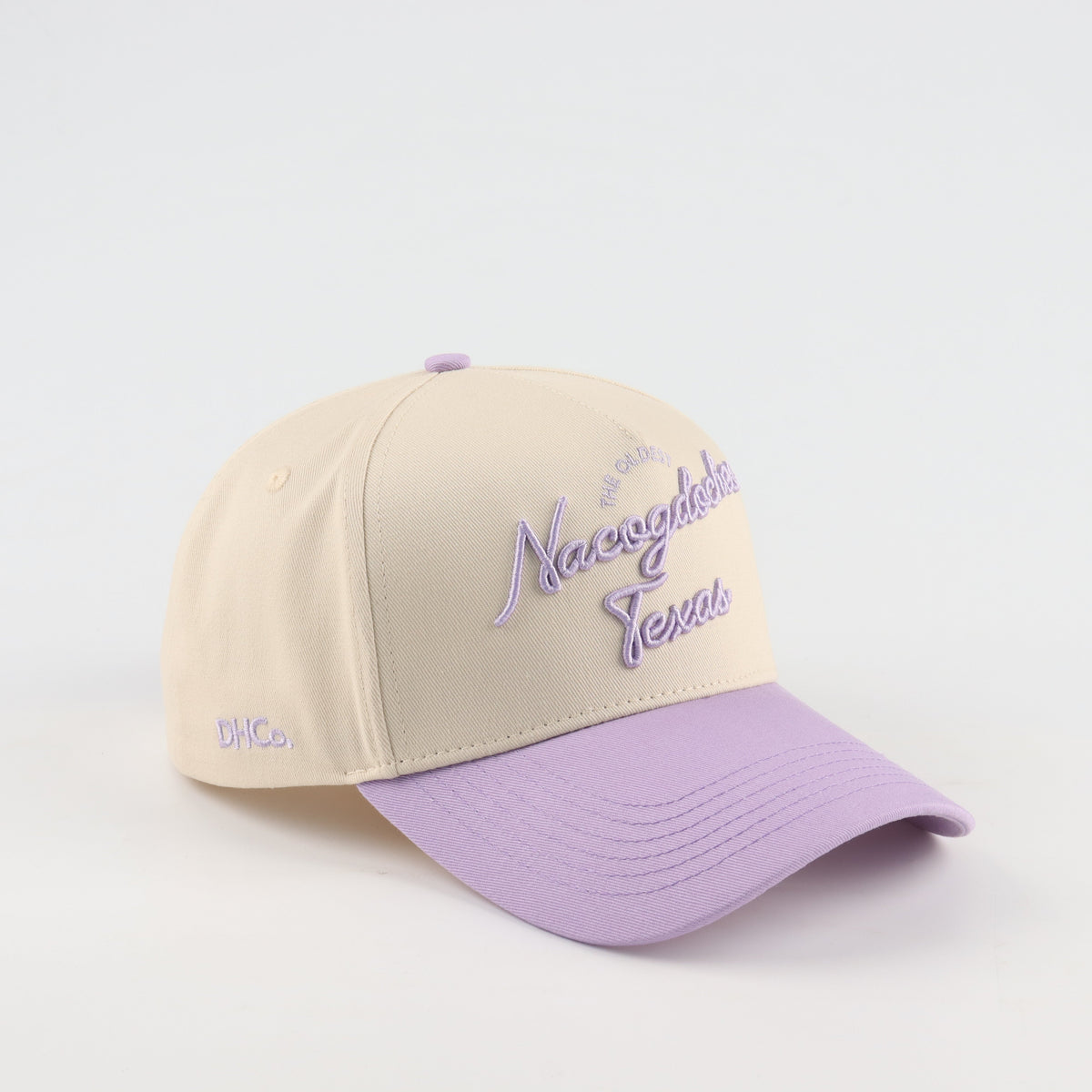 Destination Hat Co. Nacogdoches script cap with beige crown and purple bill, angled view
