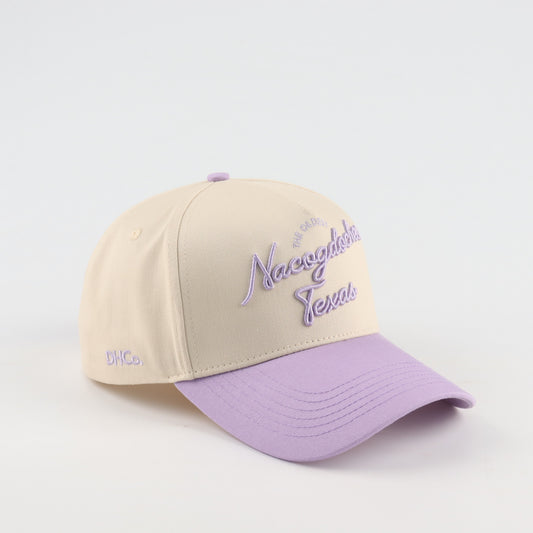 Destination Hat Co. Nacogdoches script cap with beige crown and purple bill, angled view