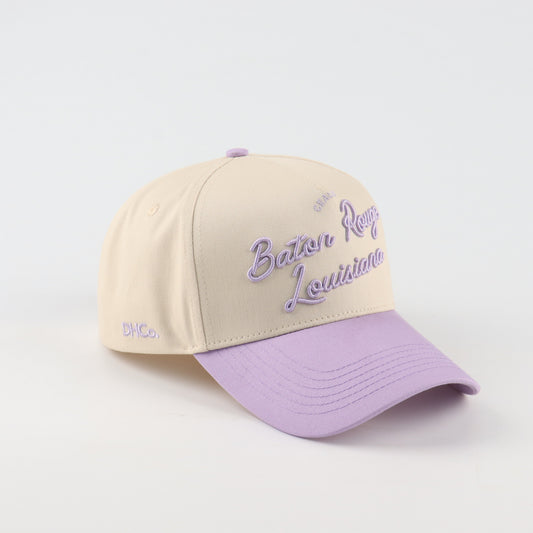 Destination Hat Co. Baton Rouge script cap with beige crown and purple bill, angled view
