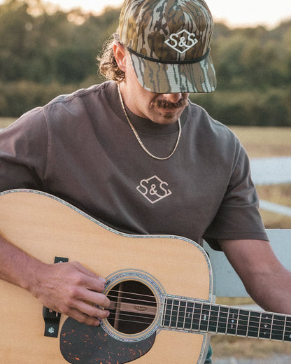 Model wearing the Bottomland Badge cap while playing guitar outdoors