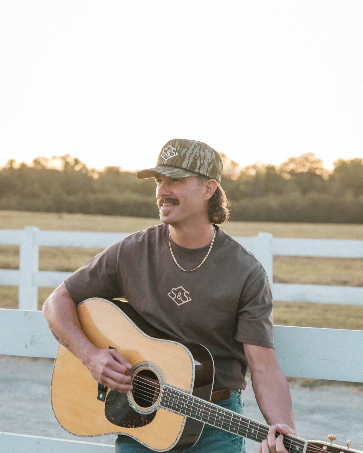 Alternate outdoor view of a model wearing the Bottomland Badge Hat with a guitar