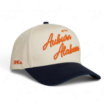 Destination Hat Co. Auburn script cap with beige crown and navy bill, angled view