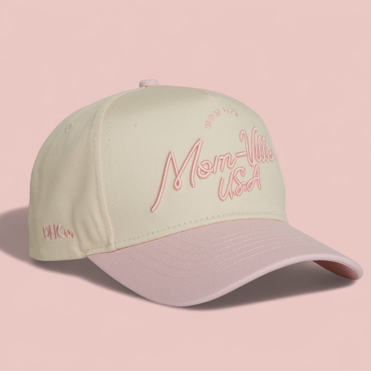 Destination Hat Co. Mom-Ville script cap with beige crown and light pink bill, angled view