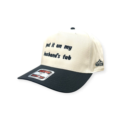Angled view of Put It on My Husband's Tab cap by Horizon Hat Co. in Natural/Black showing put it on my husband's tab front embroidery