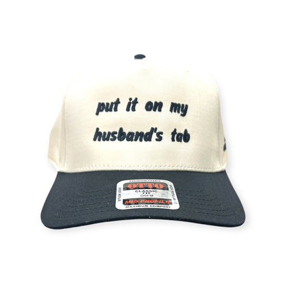 Front view of Put It on My Husband's Tab cap by Horizon Hat Co. in Natural/Black showing put it on my husband's tab front embroidery