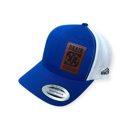 Angled view of Drain Surgeon patch hat by Horizon Hat Co. in royal/white showing the curved bill and side panels