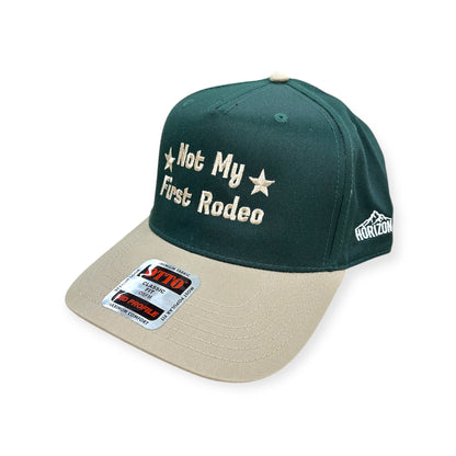 Angled view of Not My First Rodeo embroidered cap by Horizon Hat Co. in green/natural showing the bill and side panels