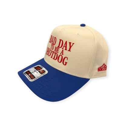 Angled view of Bad Day To Be A Hotdog patch hat by Horizon Hat Co. in natural/blue showing the bill and side panels
