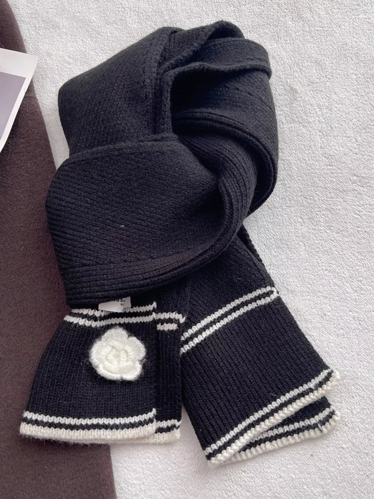 Women's Contrast Trim Knitted Scarf with Camellia Decor — black scarf tied to display pale stripes and camellia decoration