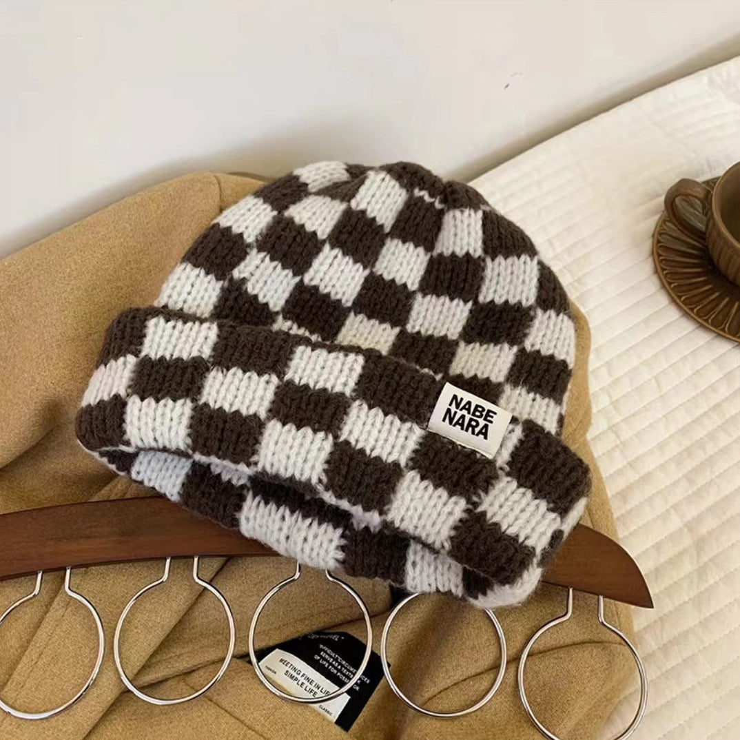 Brown and cream checkerboard knit beanie displayed on a chair