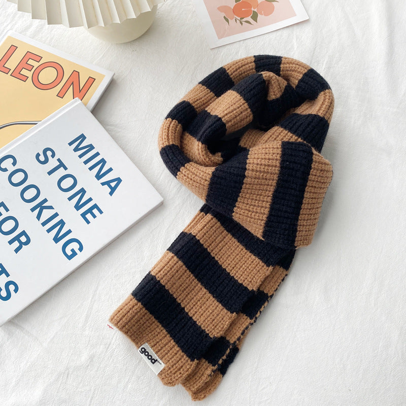 Camel and black striped knit scarf looped on a pale surface